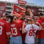 San Francisco 49ers fans cheering in red and gold jerseys while holding Christian McCaffrey, Brock Purdy, and George Kittle merchandise including trading cards and a bobblehead in front of Levi's Stadium.