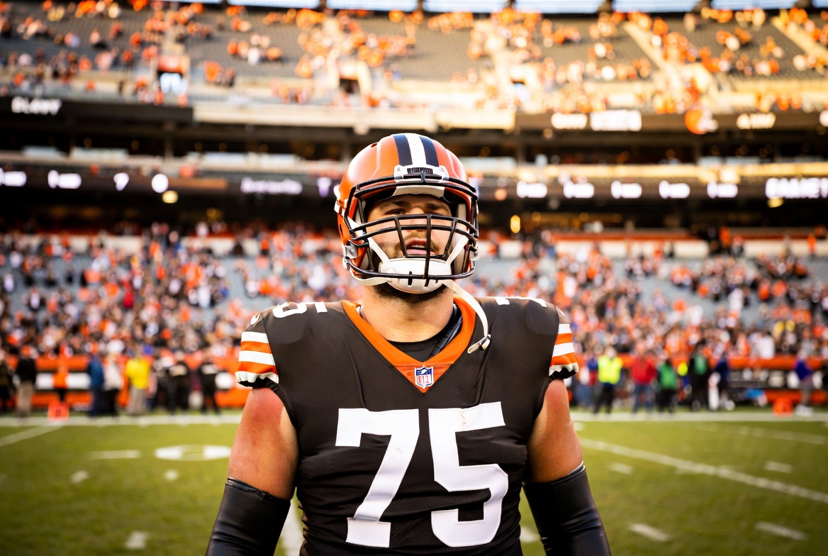 Joel Bitonio in his iconic No. 75 Cleveland Browns uniform and helmet, standing on the field at Browns Stadium with the Dawg Pound behind him, capturing quiet pride and reflection on the eve of his retirement announcement.